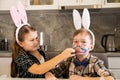 The girl paints the bunny ears face of the boy in the headband with paint using a brush. Easter Celebration