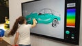 A girl paints a car on an interactive whiteboard