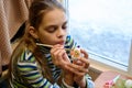 Girl paints Easter eggs while sitting at the table by the window