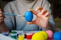 Girl paints an egg blue for the holiday at Easter. girl draws with a brush on a chicken egg Royalty Free Stock Photo