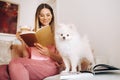 A girl in pajamas at home reads a book with her dog Spitzer, the Dog and its owner are resting on the sofa and reading a book. Royalty Free Stock Photo