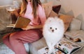 A girl in pajamas at home reads a book with her dog Spitzer, the Dog and its owner are resting on the sofa and reading a book. Royalty Free Stock Photo