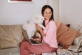 A girl in pajamas at home is working on a laptop with her dog Spitzer, the dog and its owner are resting on the couch and watching Royalty Free Stock Photo