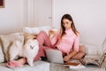 A girl in pajamas at home is working on a laptop with her dog Spitzer, the dog and its owner are resting on the couch and watching Royalty Free Stock Photo