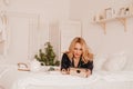 A girl in pajamas lies on the bed with a tablet. Morning news check. Home Office. Work during quarantine. Royalty Free Stock Photo