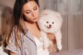 A girl in pajamas sits in bed at night with her white dog watching a laptop and eating sweets.Girl with a dog Spitzer at home in Royalty Free Stock Photo