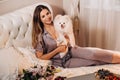 A girl in pajamas sits in bed at night with her white dog watching a laptop and eating sweets.Girl with a dog Spitzer at home in Royalty Free Stock Photo