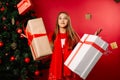 The girl is in pajamas by Xmas tree, with a bunch of gifts in the air. Superhero- women power. Photo on red background.