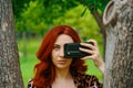 Red-haired woman takes a picture on her phone.