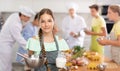 Girl participant in culinary master class is standing with bowl and carafe of milk in hands.