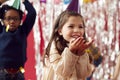 Girl In Party Hat Celebrating At Birthday Party Blowing Handful Of Gold Confetti And Glitter