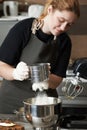 The girl pastry chef pours flour through a sieve into the bowl of a mixer