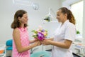 Girl patient gives a bouquet of flowers to a female doctor in dental office. National dentist`s day.
