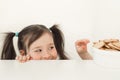 A girl peeks out from the table. The child wants to steal cookies. Funny baby hunts for delicious cookies