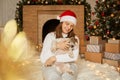 Girl with Pekingese dog on background of Christmas decorations and fireplace, woman with puppy sitting on floor on soft carpet,