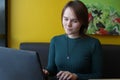 A girl with a pensive tense interested expression on her face sits, working at a laptop at a table in a cafe on a brown