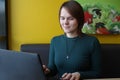 A girl with a pensive tense interested expression on her face sits, working at a laptop at a table in a cafe on a brown