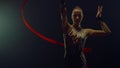 Girl performing with flying ribbon for camera. Gymnast rehearsing in dark hall.