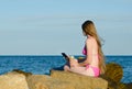 Girl with the phone sitting on the rocks in a bathing suit against the sea Royalty Free Stock Photo