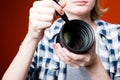 Girl photographer cleans lens of professional SLR camera after a long shoot in the Studio with red background.