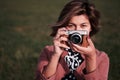 Girl photographer with mirrorless camera like old camera looks to the camera with a green background