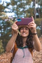 A woman in a hat and with a backpack walks along a forest path and takes a selfie