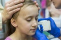 Girl pierced ear in the beauty salon. Adorable little girl having ear piercing process with special equipment in beauty center by Royalty Free Stock Photo