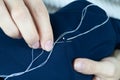 The girl pierces the fabric with a needle to make a stitch. White thread on blue fabric. Needlework, homecraft, DIY Royalty Free Stock Photo