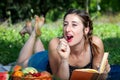 Girl with pigtails lying on the grass, reading a book and eating fruit, during a picnic in the park Royalty Free Stock Photo