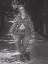 A girl with pigtails in a plaid shirt and very wide jeans stands in a curtsy pose in an alley in a park. Black and white Royalty Free Stock Photo