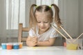 Girl with pigtails sits on a chair and paints the sun with a brush with yellow paint Royalty Free Stock Photo