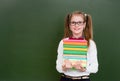 Girl with a pile books near empty green chalkboard