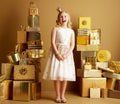 Girl among 2 piles of golden gifts in front of plain wall