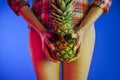 A girl with a pineapple in his hands holds him between slender legs, bright neon lights