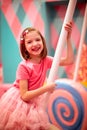 Girl in pink clothes with a Lollipop. In the background, a variety of sweets.