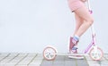 Girl in pink clothes rides on a pink scooter on the background of a white wall Royalty Free Stock Photo