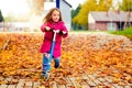 Girl in pink coat is riding scooter on maple leaves. Royalty Free Stock Photo