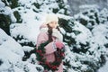 Girl in pink coat in snow Park. Girl plays in winter Park. Adorable child walking in snow winter forest touch wood branch on tree. Royalty Free Stock Photo