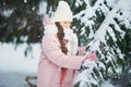 Girl in pink coat in snow Park. Girl plays in winter Park. Adorable child walking in snow winter forest touch wood branch on tree. Royalty Free Stock Photo