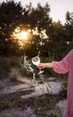 A girl in a pink dress holds a beautiful glass of water and flowers in the setting sun. Glare, summer, nature. Royalty Free Stock Photo