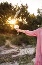 A girl in a pink dress holds a beautiful glass of water and flowers in the setting sun. Glare, summer, nature. Royalty Free Stock Photo