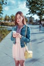 Girl pink dress, summer city park, holding mobile phone in her hand, reading message, writing text on social networks Royalty Free Stock Photo