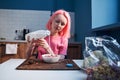 Girl with pink hair pouring milk into the plate with corn flakes