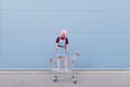 Girl with pink hair stands in a cart for shopping on the background of a blue wall Royalty Free Stock Photo