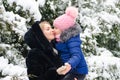 A girl in a pink hat hugs her mother against the background of trees in the snow Royalty Free Stock Photo