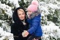 A girl in a pink hat hugs her mother against the background of trees in the snow Royalty Free Stock Photo