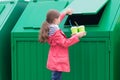 A girl in a pink jacket carries disposable glasses with tubes in a dumpster to throw them away Royalty Free Stock Photo