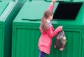 A girl in a pink raincoat brought a bag of garbage and throws it open the container