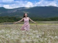 Girl in pink sleeveless dress walks on meadow of chamomile