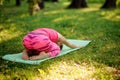 Girl in the pink sportsuit practice yoga in the park in Child`s Pose